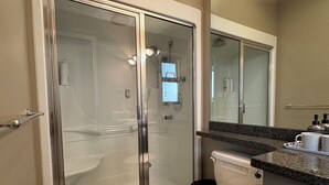 Et moderne badeværelse med et glasafskærmet brusebad, et hvidt toilet og en bordplade i granit med toiletartikler.