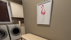 Et vaskerum med to vaskemaskiner, et træbord med bænke og et billede af en flamingo i ramme på væggen.