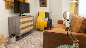Una sala de estar con televisor, sofá, sillón, lámpara y un adorno en la pared.