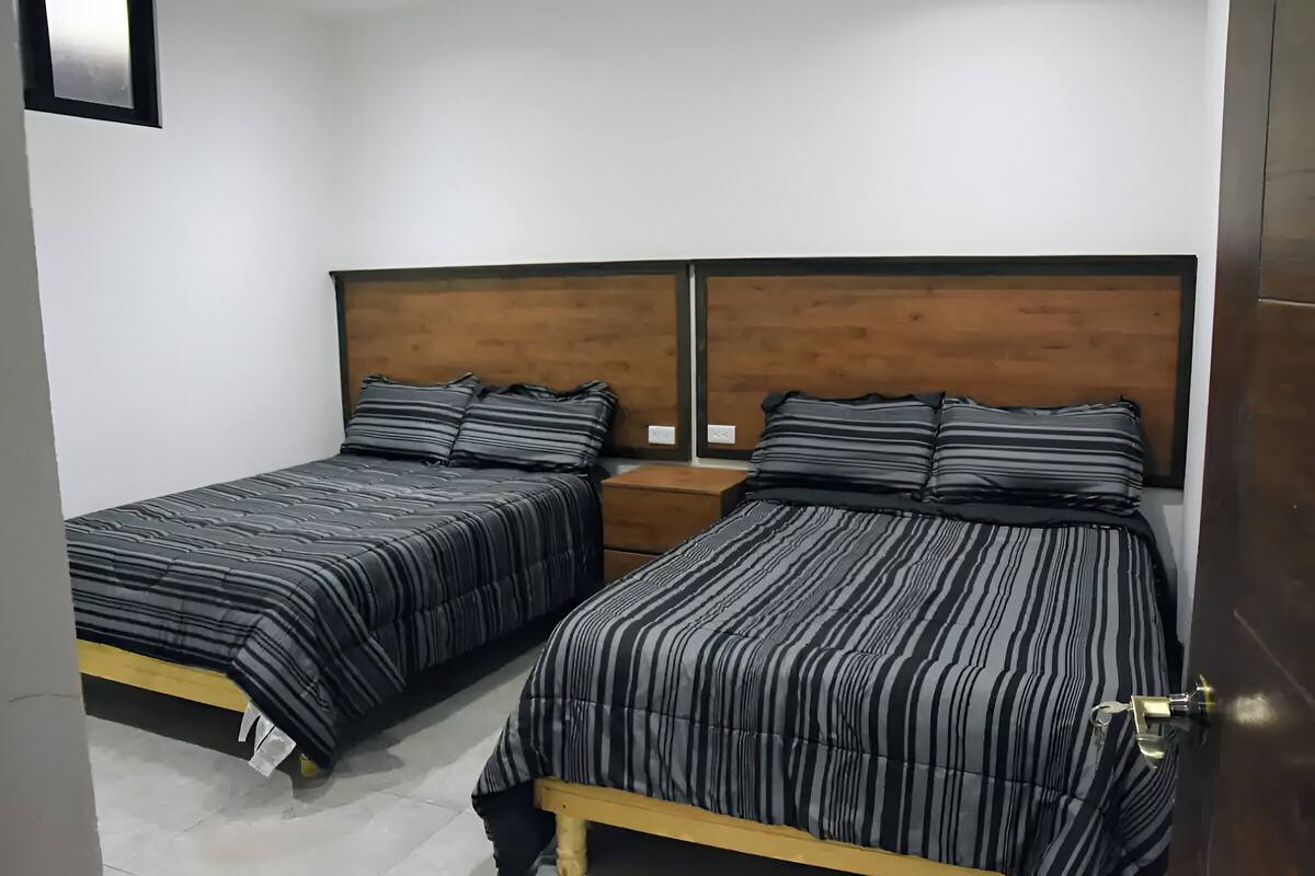 Habitación con dos camas, cada una con cabecero de madera y ropa de cama a rayas negras.