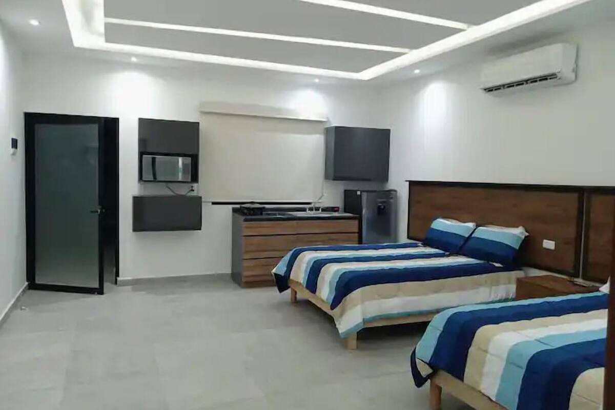 Un dormitorio moderno con dos camas, un tocador, un televisor y un equipo de aire acondicionado.