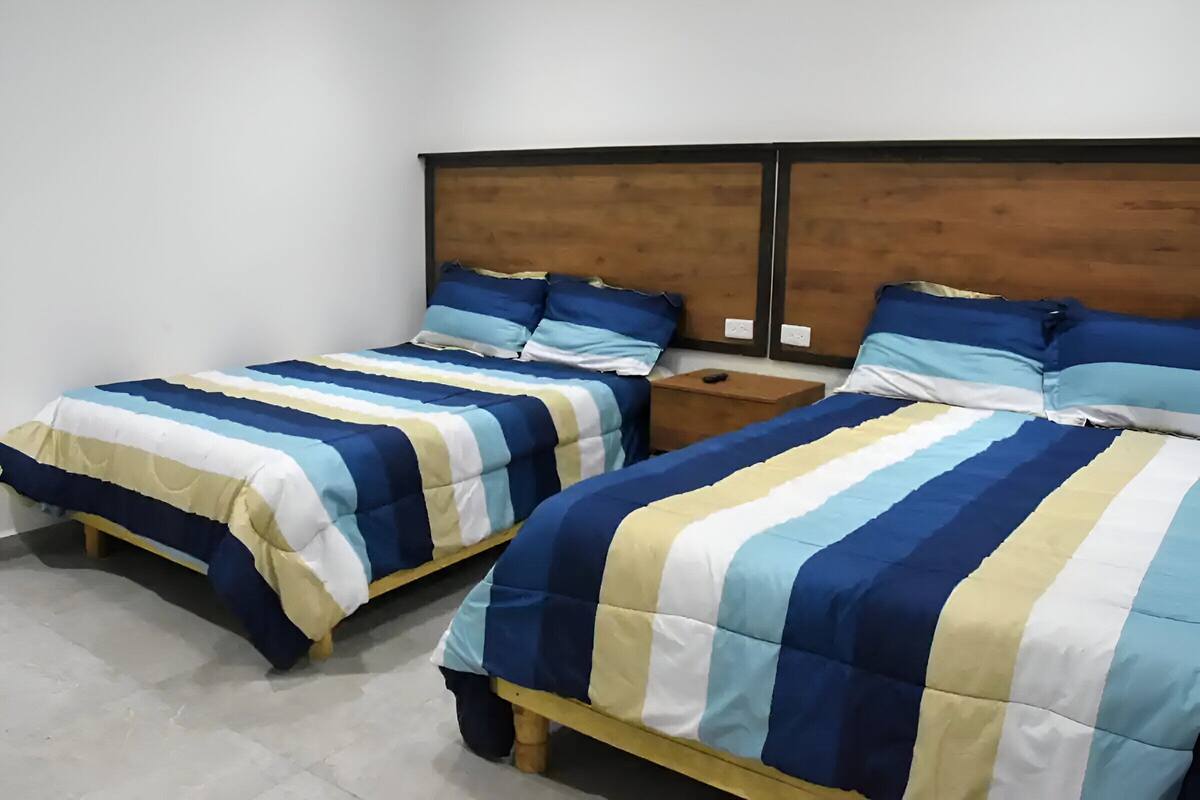 Dos camas individuales con ropa de cama a rayas, cabeceros de madera y mesitas de noche.