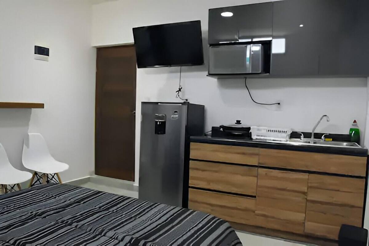 Una habitación de hotel moderna con una cama, una kitchenette pequeña, un televisor montado sobre la encimera y una puerta.