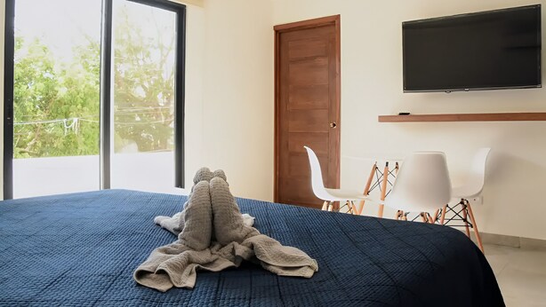 A bedroom with a large bed, a TV mounted on the wall, and a sliding glass door leading to a balcony. - MARAZUL-HOME (Playa del Carmen)