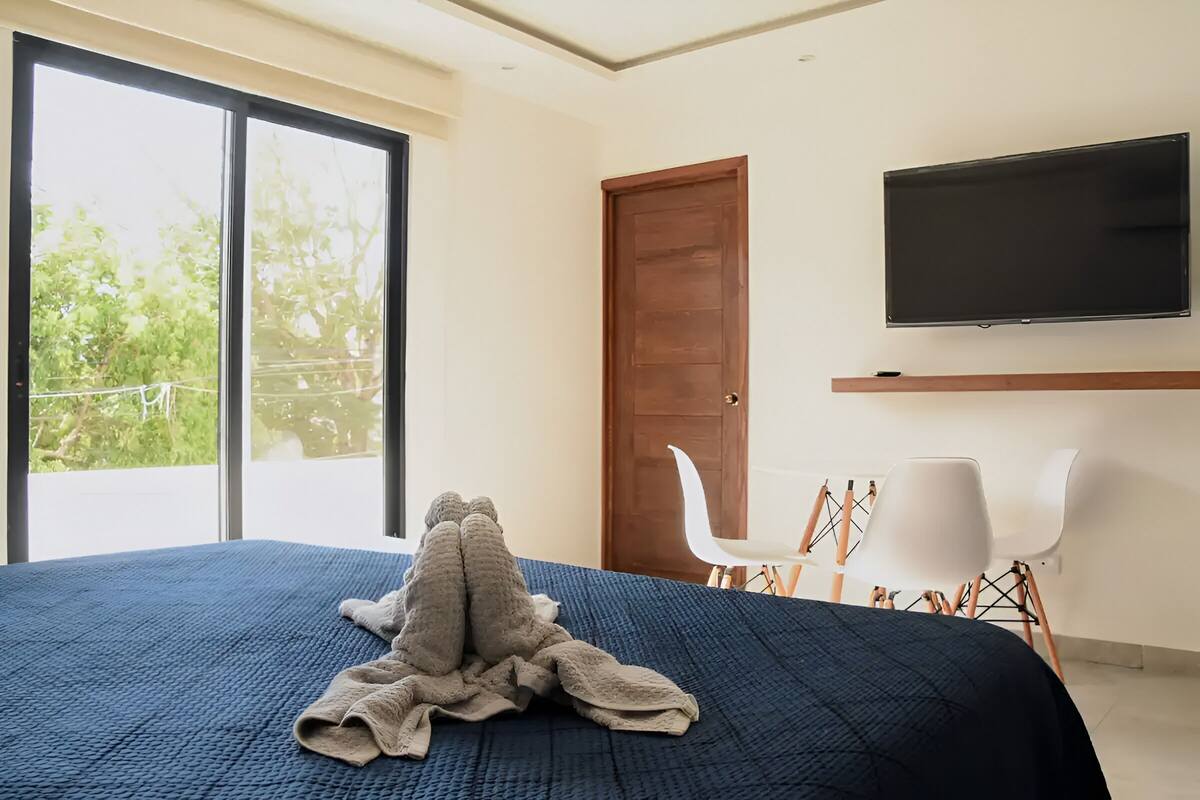 Un dormitorio con una cama grande, un televisor montado en la pared y un ventanal corredero que da a un balcón.