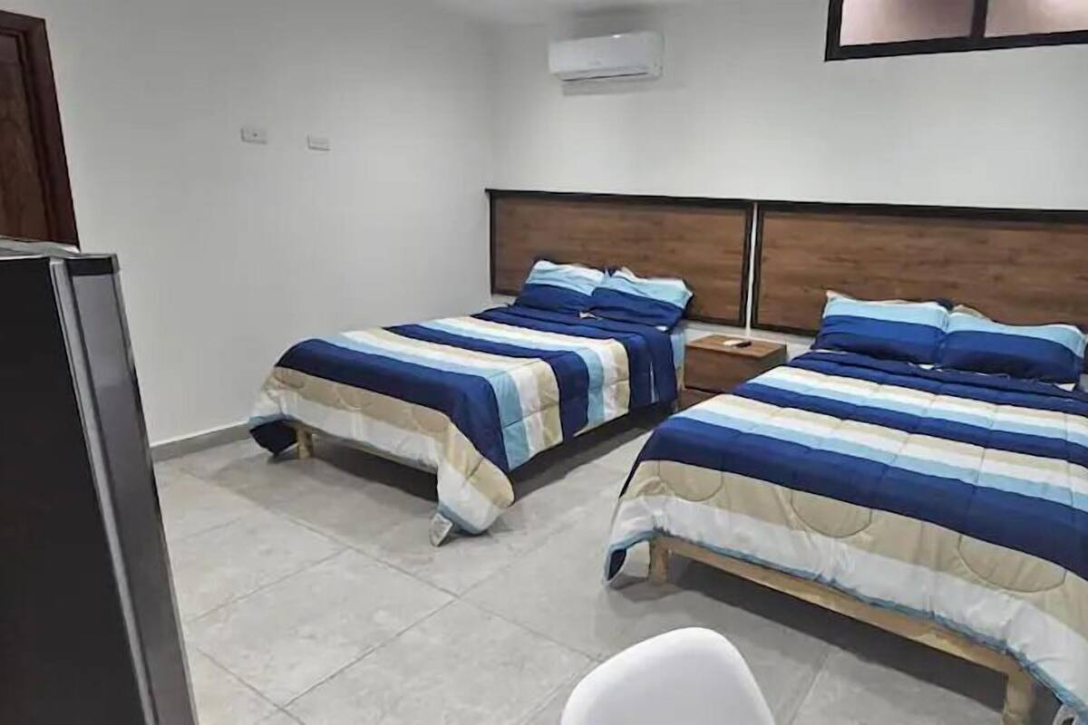 Habitación de hotel con dos camas, una mesita, una silla y un televisor.