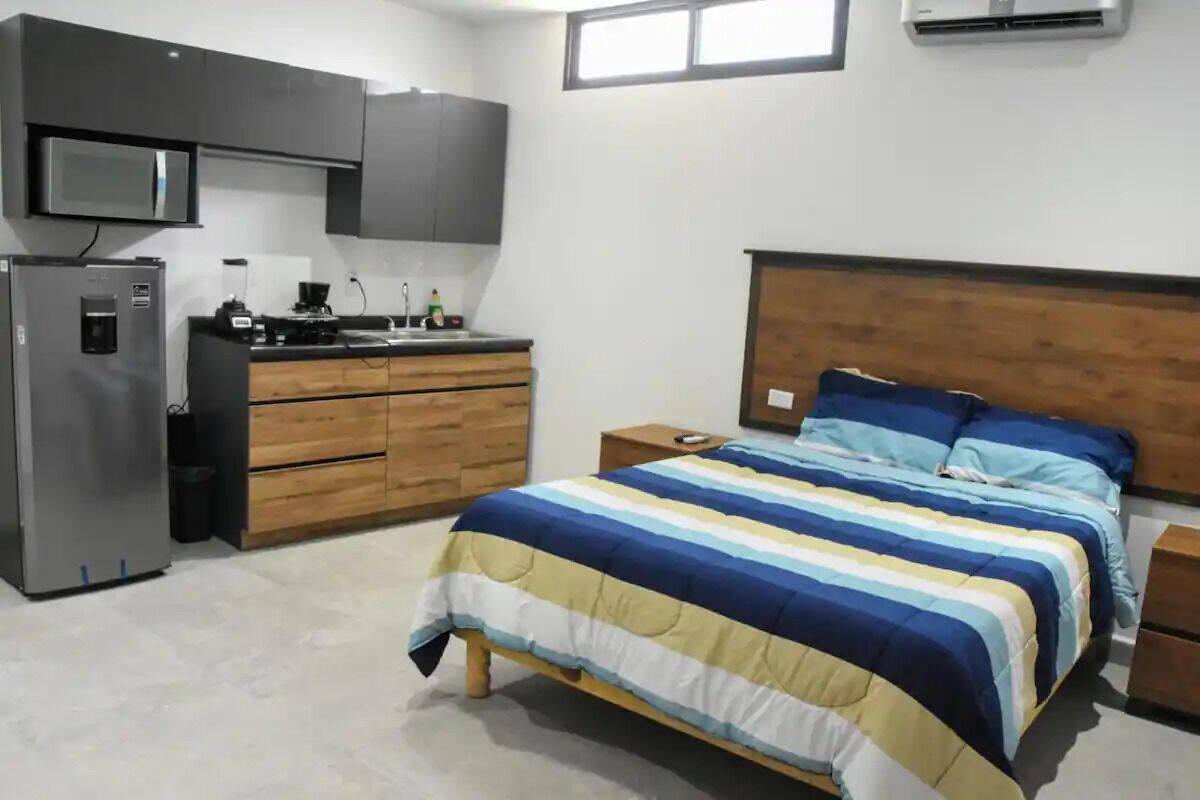 Un dormitorio con cama, cabecera de madera, mesitas de noche y una pequeña mesita auxiliar.