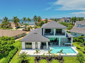Ein zweistöckiges Haus mit Swimmingpool, umgeben von Palmen und Blick auf den Ozean.