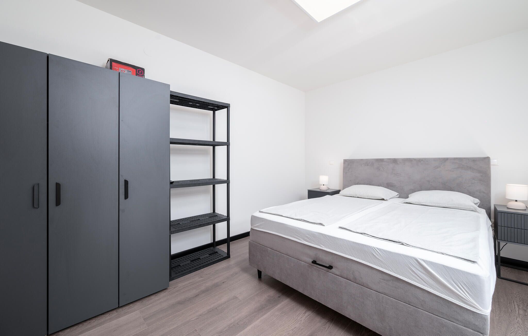A modern bedroom with a grey wardrobe, a bed with grey bedding, and a skylight above.