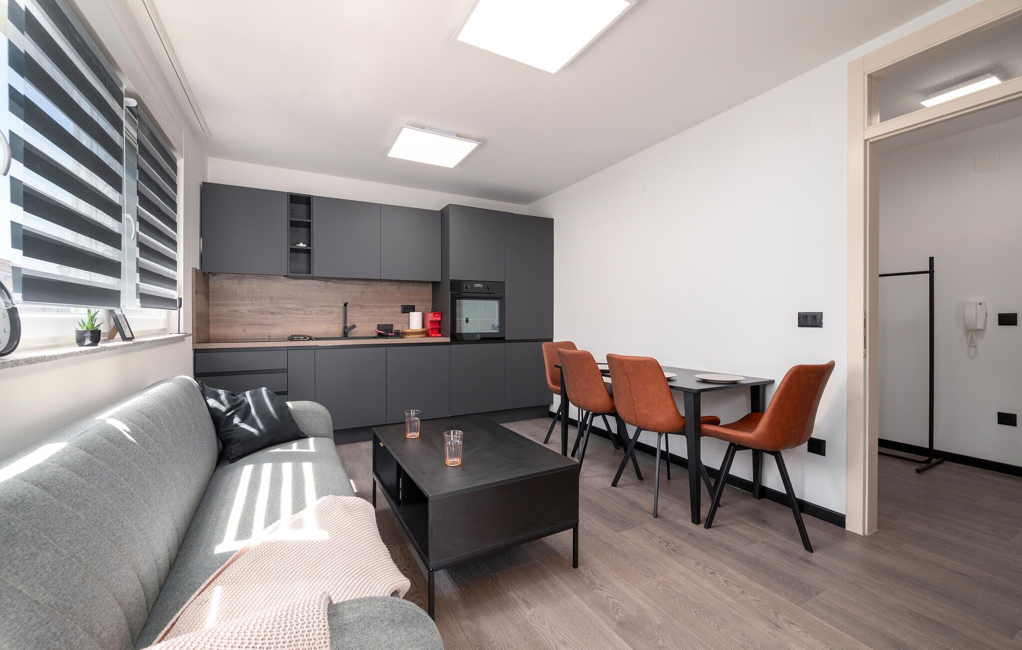 Une cuisine moderne avec des meubles gris, un four encastré et un coin repas comprenant une table et des chaises.