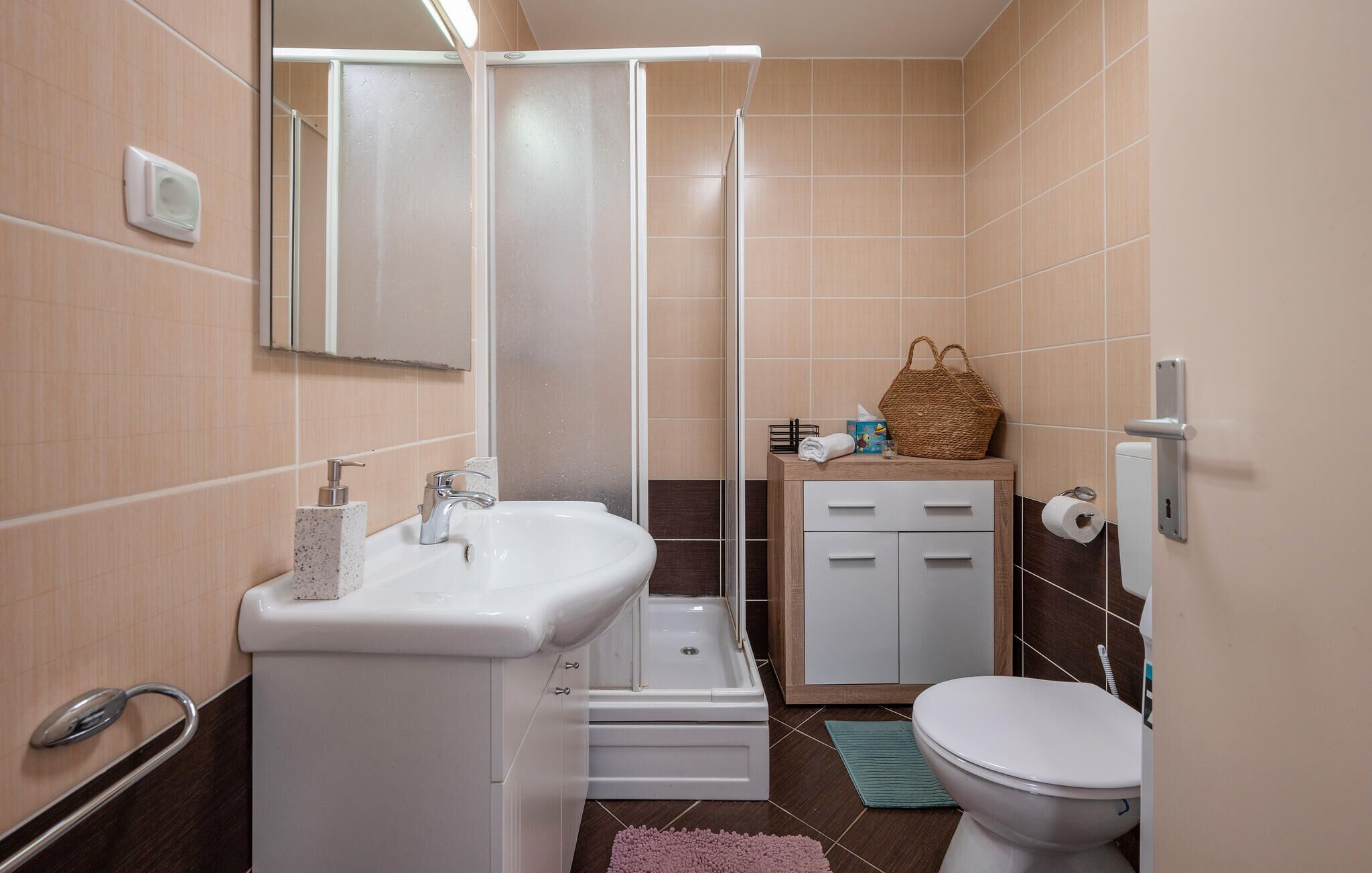 Une salle de bain équipée d’une douche, d’un lavabo, de toilettes et d’un petit meuble contenant des articles de toilette.