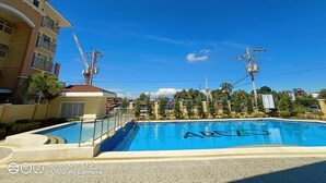 A swimming pool with a clear blue sky above, surrounded by buildings and power lines. - Cozy & Quiet 1 BR Condo w/ Free Pool Access Near Beach, Airport and Malls (Davao City)