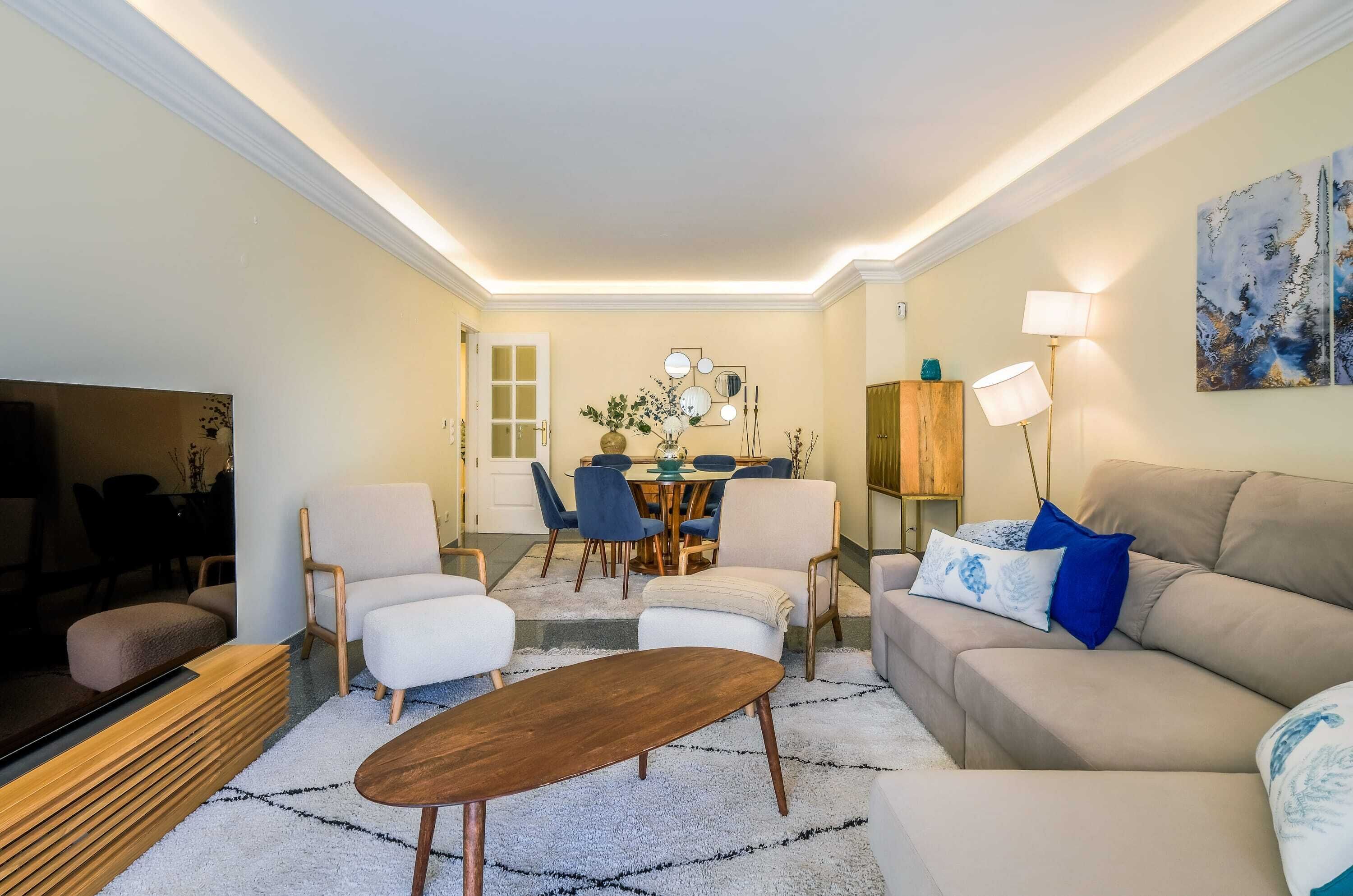 A living room with a sofa, chairs, a coffee table, a TV, and a dining area with a table and chairs.
