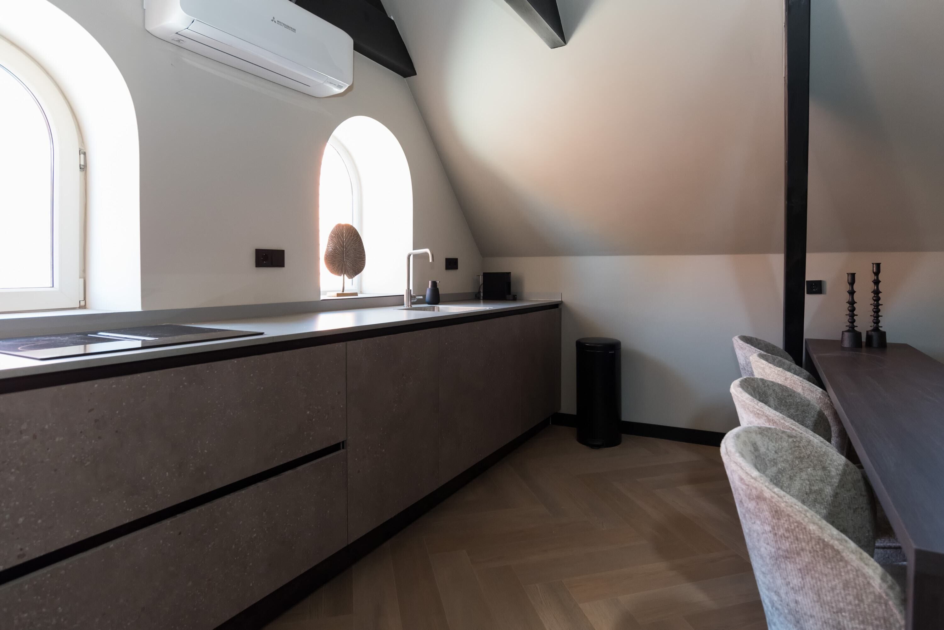 A modern kitchen with a large island, two windows, and a black trash bin.