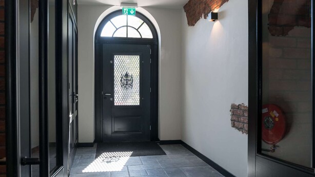 A hallway with a black door, a white wall, and a brick accent. - De Vooruitgang Sneek - de Zwette (Sneek)
