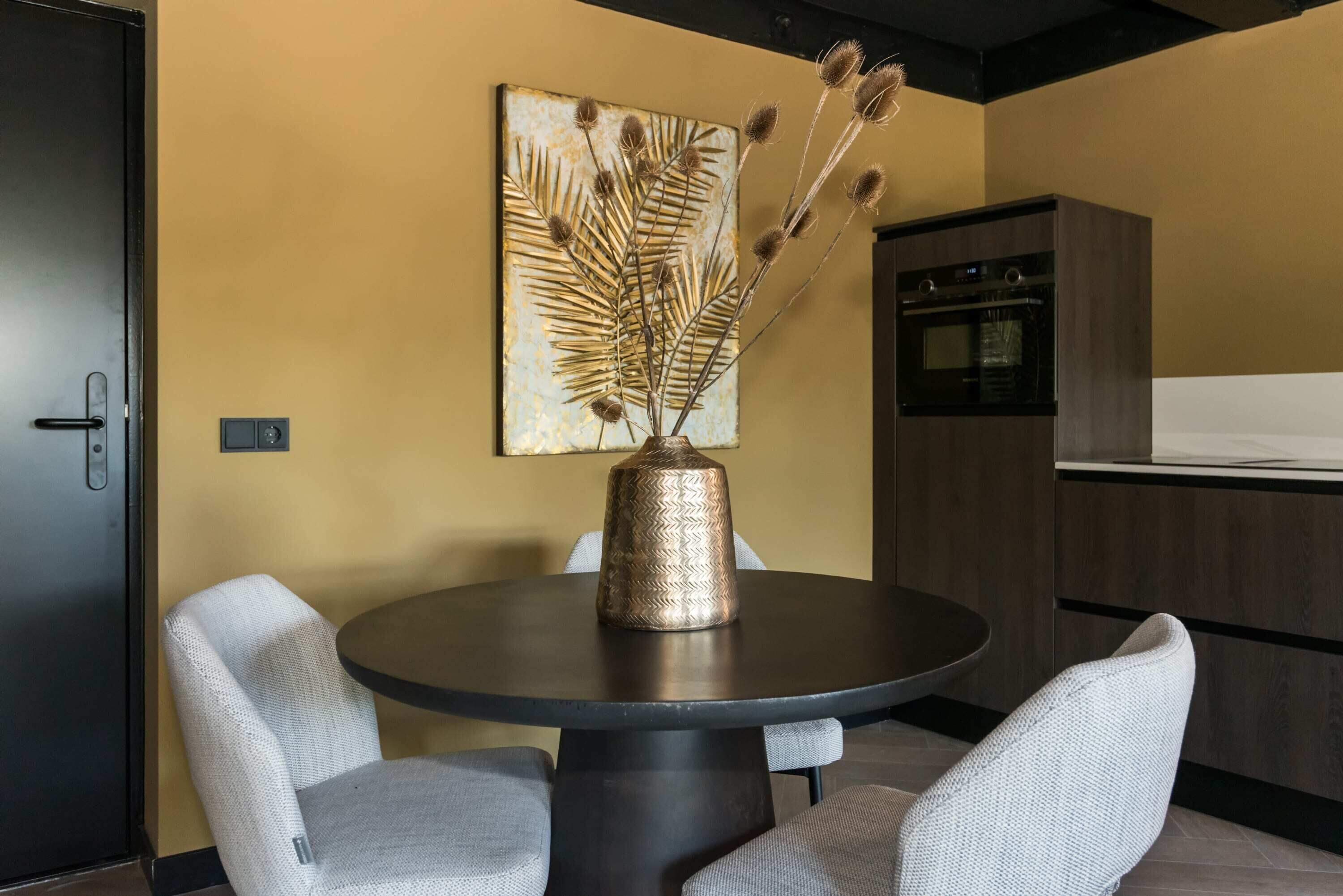 Uma área de refeições com uma mesa redonda, duas cadeiras, um vaso decorativo e um quadro pendurado na parede.
