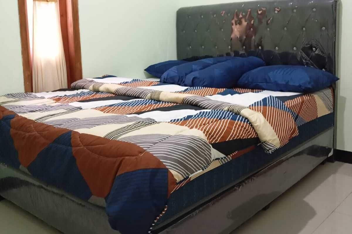 Una cama con colcha a rayas, cabecera tapizada de gris y una ventana con cortinas.