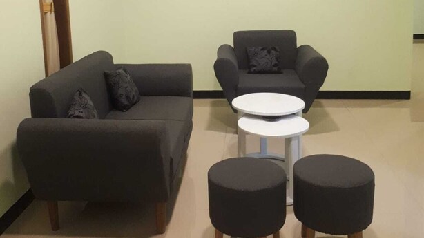 A modern living room with a sofa, armchair, ottomans, and a small round table. - Dhea Homestay Bromo (Ngadisari)