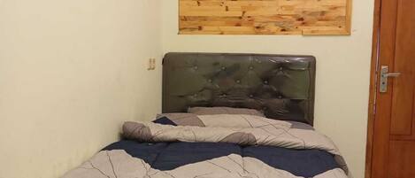 A small, neatly made bed with a geometric-patterned bedspread in a room with a wooden wall panel and a door.