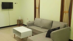 A living room with a sofa, a coffee table, a TV, and curtains. - Dhea Homestay Bromo (Ngadisari)