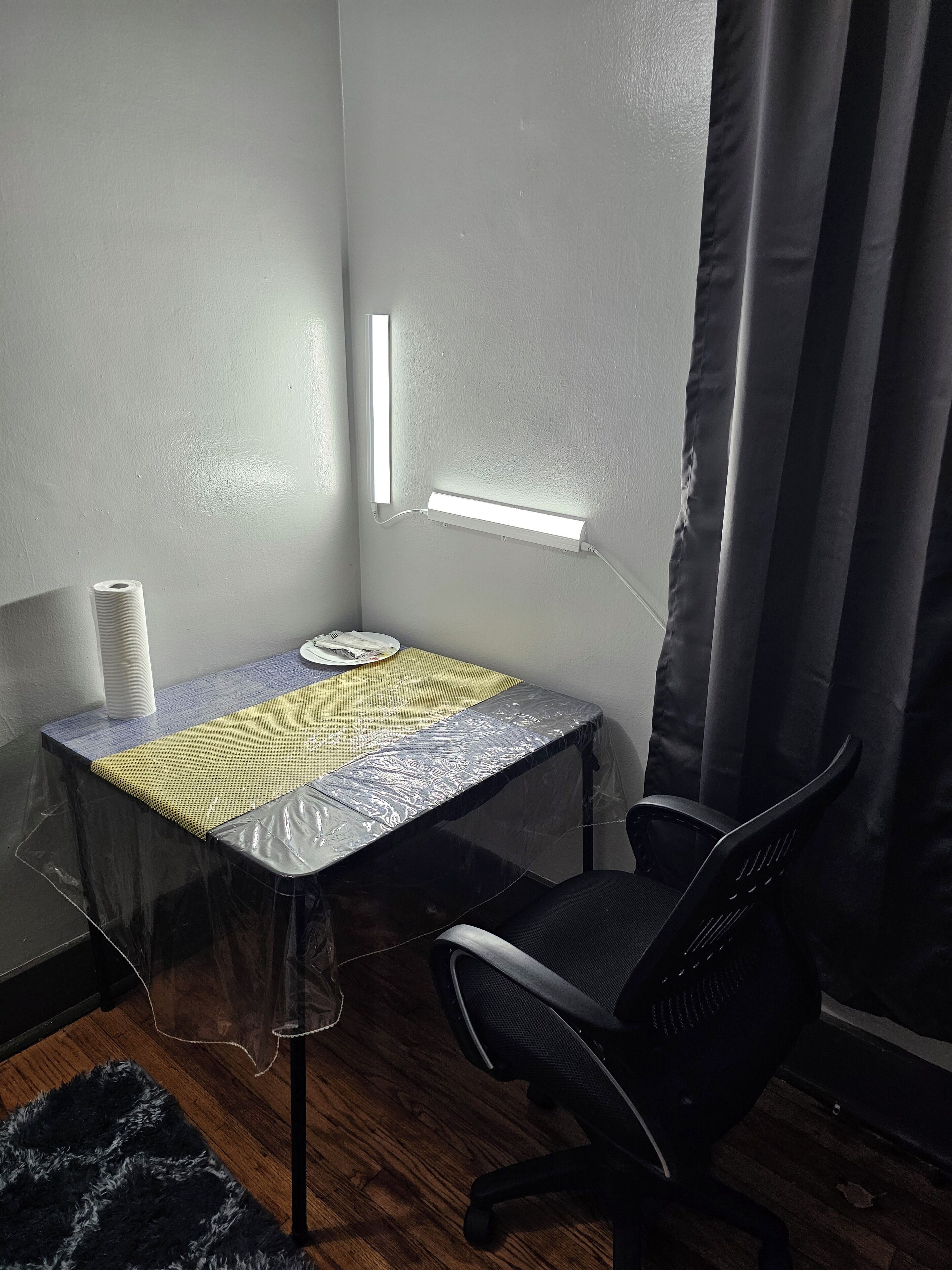 A small, enclosed workspace with a desk, chair, and a wall-mounted light.
