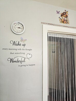 Una pared con un reloj, una cita decorativa y un comedero para pájaros con mariposas.