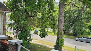A residential street with a brick house, a metal railing, and a car parked on the street.