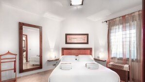 Un dormitorio amplio con una cama grande, un cabecero de madera, una mesita de noche con lámpara y un espejo grande en la pared.