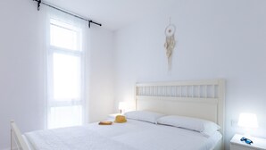 A neatly made bed with a white headboard, a bedside table with a lamp, and a wall hanging.