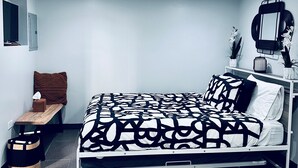 A bedroom with a bed, bedside table, lamp, mirror, and a small bench.