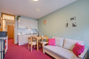 A compact living space with a kitchenette, a dining area, and a sofa with a red pillow.
