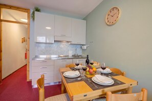 A compact kitchen with white cabinets, a marble backsplash, and a dining area with a table set for two. - Studio Valleverde 4d (Sestriere)