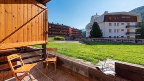 Ein Holzbauten mit Balkon, eine Rasenfläche und ein weißes Gebäude mit Balkonen im Hintergrund.