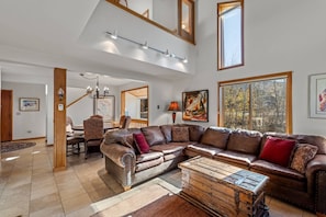 A spacious living room with a large sectional sofa, a wooden coffee table, and a dining area with a chandelier.
