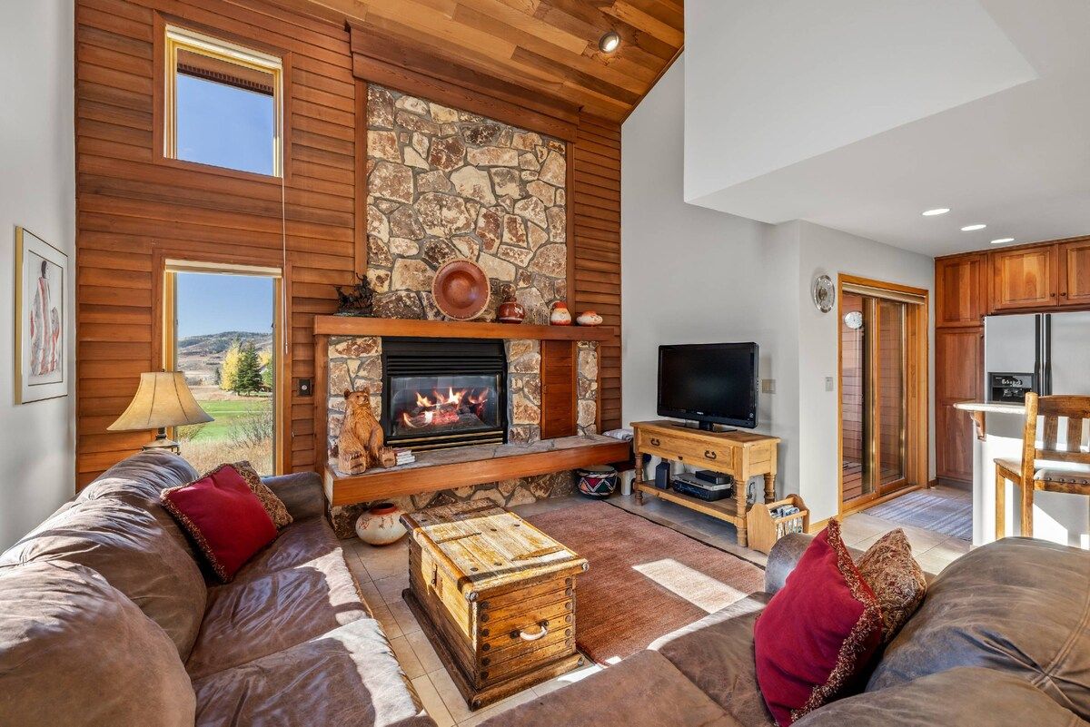 Una sala de estar con chimenea de piedra, techo de madera y un televisor sobre un mueble de madera.