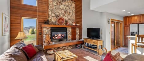 Una sala de estar con chimenea de piedra, techo de madera y un televisor sobre un mueble de madera.