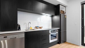 A modern kitchen with black cabinets, a stainless steel dishwasher, a built-in oven, and a refrigerator. - Central City Abode on St Asaph (Christchurch)