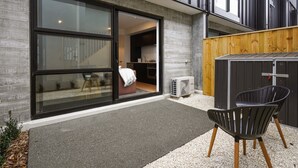 A modern house with a sliding glass door leading to a kitchen, a small outdoor seating area with a chair, and a wooden fence. - Central City Abode on St Asaph (Christchurch)