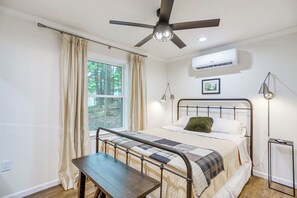 Ein Schlafzimmer mit einem Bett, einem Deckenventilator, einer Klimaanlage, einem Fenster mit Vorhängen und einem Nachttisch.