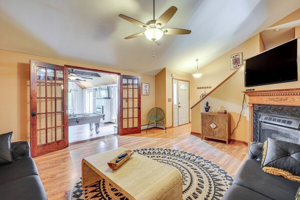 A spacious living room with hardwood floors, a ceiling fan, a fireplace, a television, and a large window. - Game Room & Private Yard: Family Gem in Kunkletown (Kunkletown)