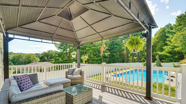 Eine überdachte Terrasse mit Korbmöbeln, einem Glastisch und Blick auf einen Swimmingpool.