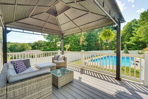 A covered deck with wicker furniture, a glass-top table, and a view of a swimming pool. - Game Room & Private Yard: Family Gem in Kunkletown (Kunkletown)