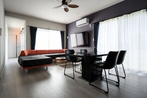 A modern living room with a sofa, dining table, chairs, and a ceiling fan. - Orange House (Miyakojima)