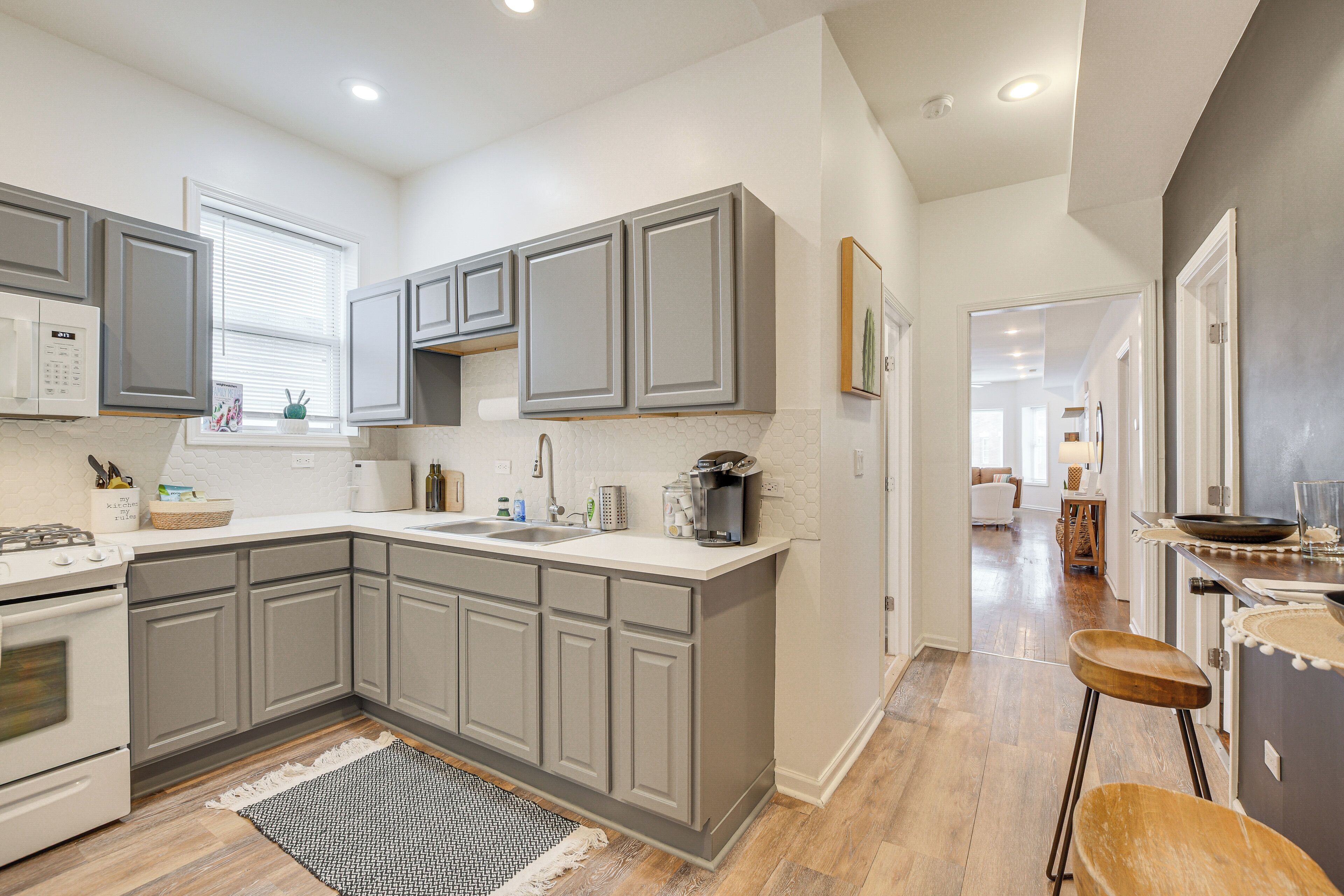 A modern kitchen with grey cabinets, a white countertop, and a wooden floor.