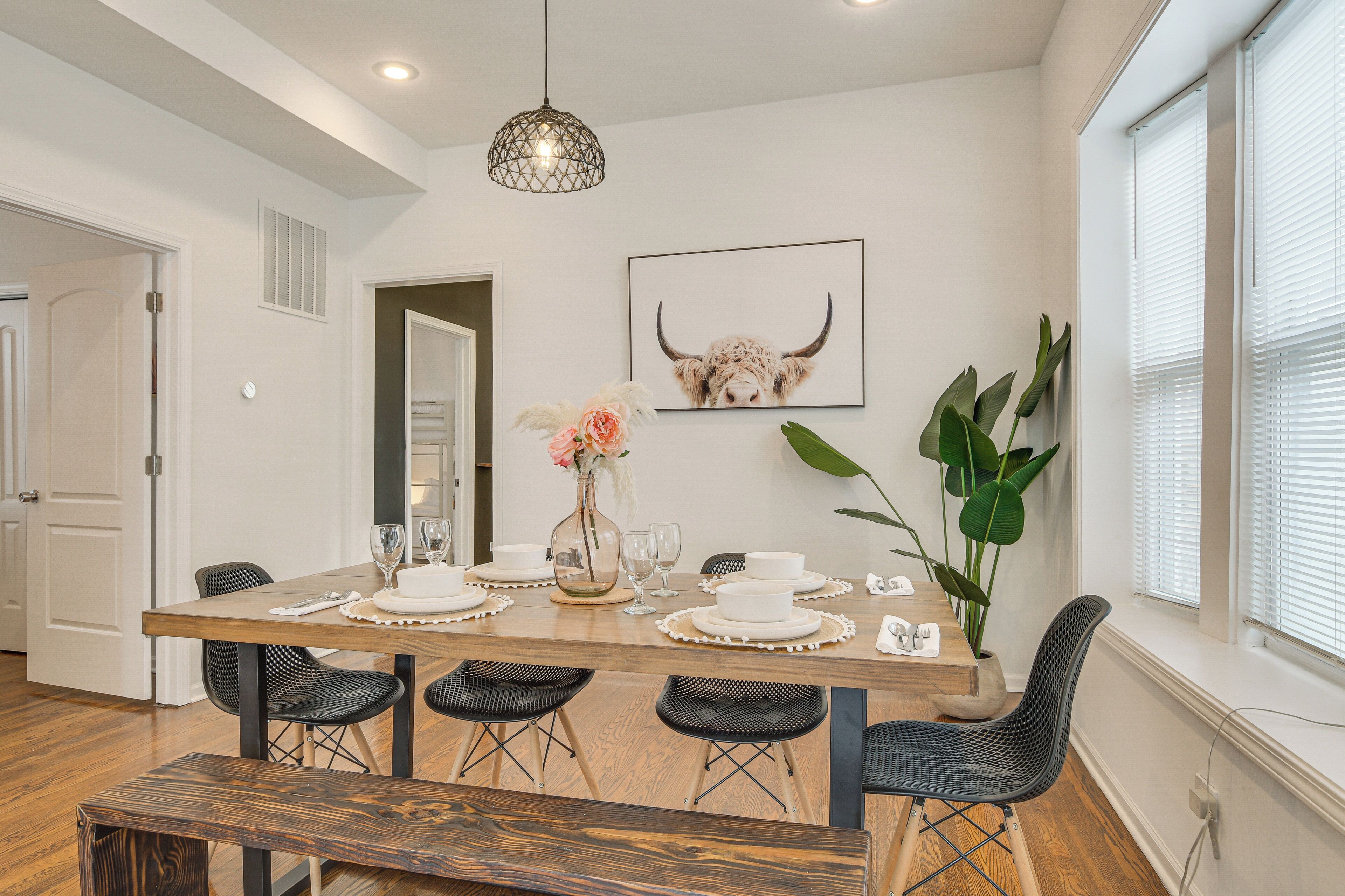 A dining area with a wooden table set for four, surrounded by black chairs, a vase with flowers, and a framed picture on the wall.