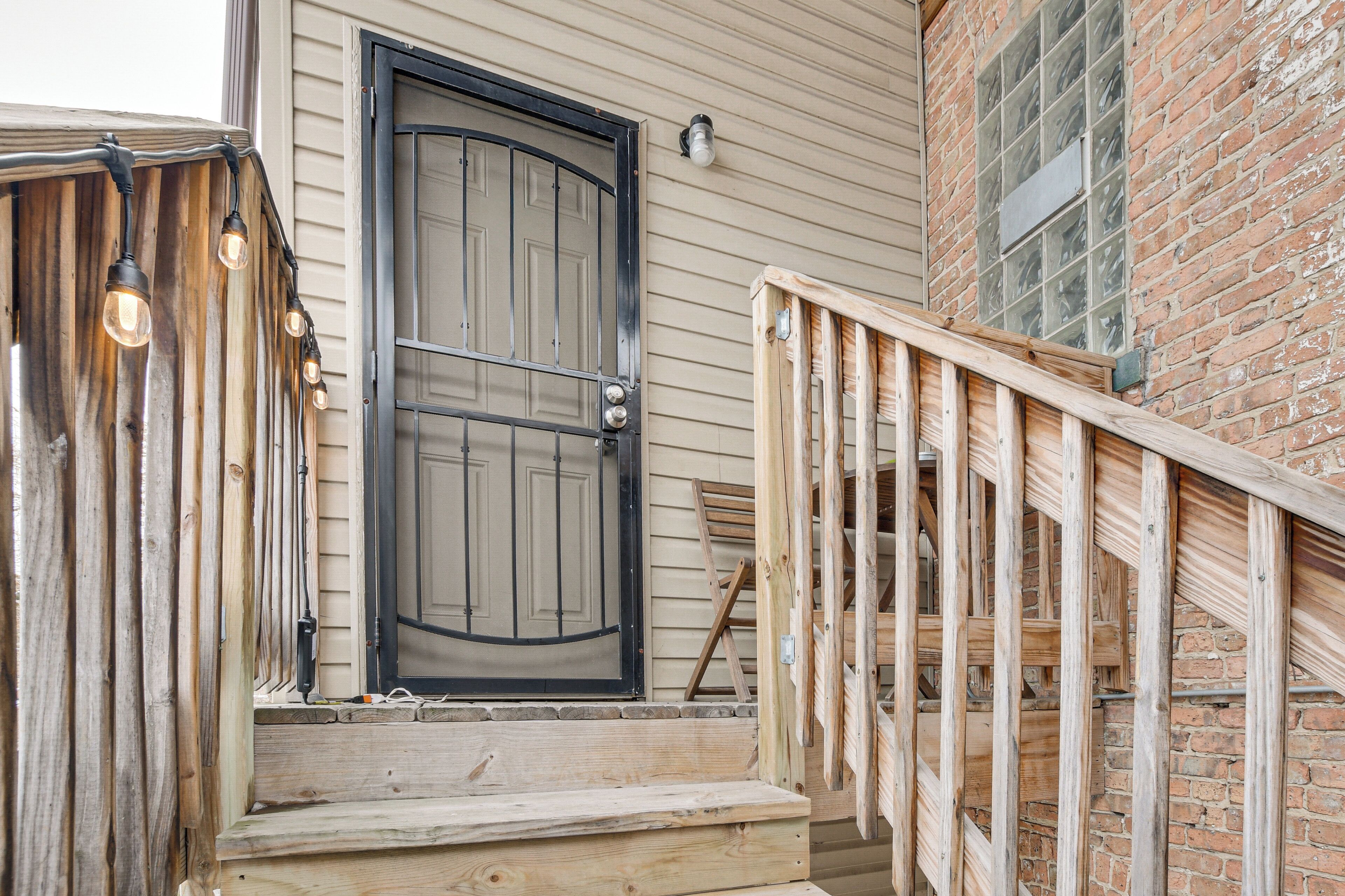 A wooden staircase leading to a door with a black frame, a brick wall, and a window with multiple panes.