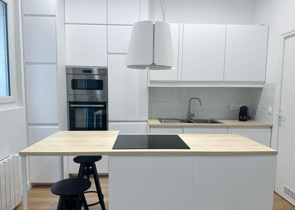 A modern kitchen with white cabinetry, a built-in oven, a sink, and a black countertop.