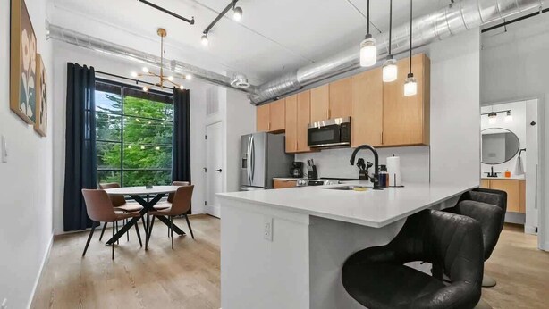 A modern kitchen with a central island, wooden cabinets, stainless steel appliances, and pendant lighting. - Hot Tubs I 2 King BR I Condo I Near DT TC (Traverse City)