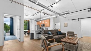 A modern living room with a sofa, chairs, and a coffee table. There is a kitchen in the background with a microwave and cabinets. - Hot Tubs I 2 King BR I Condo I Near DT TC (Traverse City)