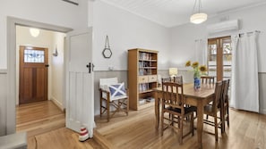 A dining area with a wooden table and chairs, a bookshelf, and a door with a stained glass window. - Maison Cottage in Queenscliff (Queenscliff)